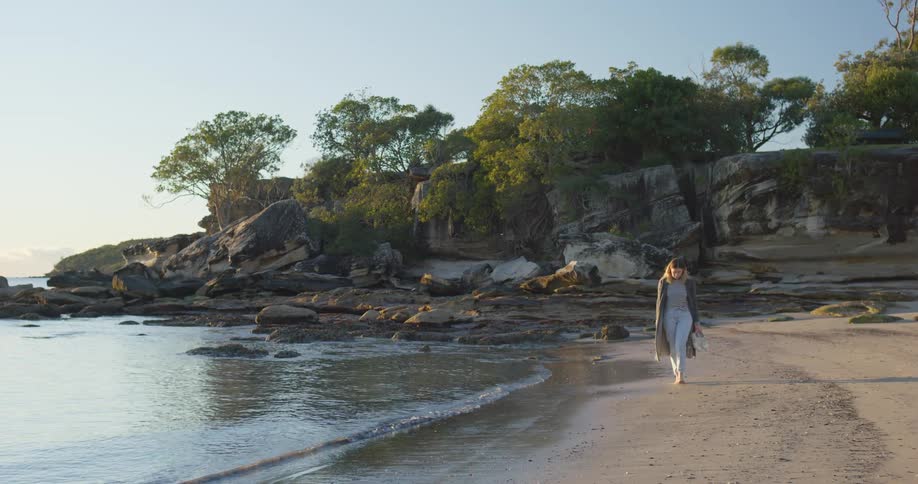 A woman walking barefoot alone on a sandy beach