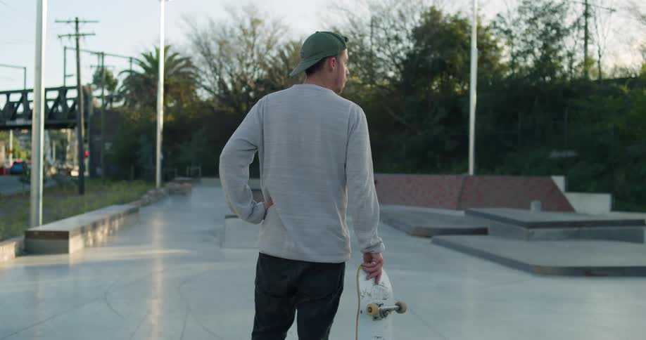 Young man holding a skateboard stands in a skate park at evening
