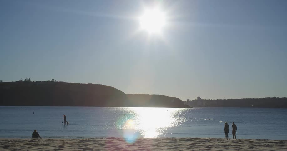 People are on a beach looking at the water as a person on a sup board paddles by