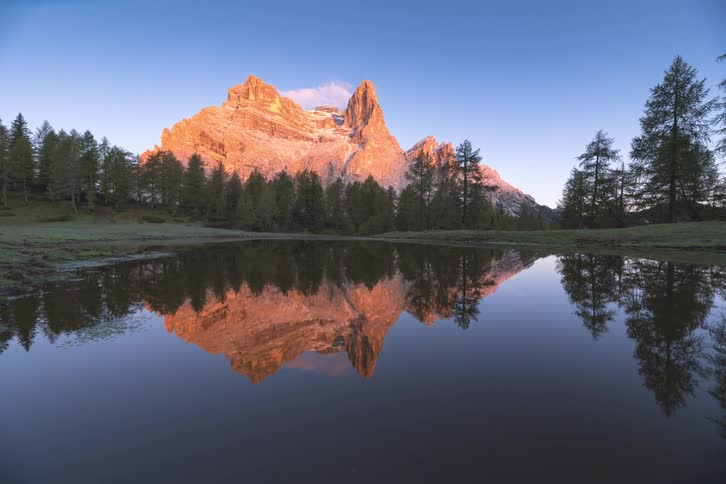 A lake surrounded by pine trees and the mountain in the distance are reflecting onto the water