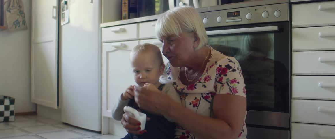 A grandmother holding her baby grandchild on a kitchen floor at home