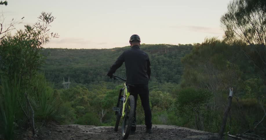 A man standing with a mountain bike overlooking trees and hills