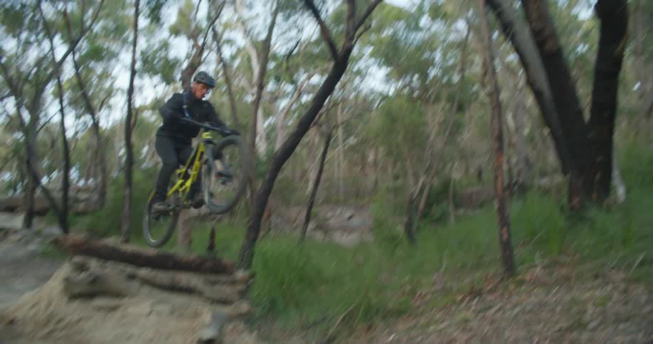 A man mountain biking in a forest goes over a ramp