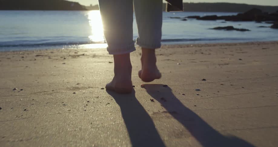 A person is approaching the sea as footsteps can be seen walking on the sand