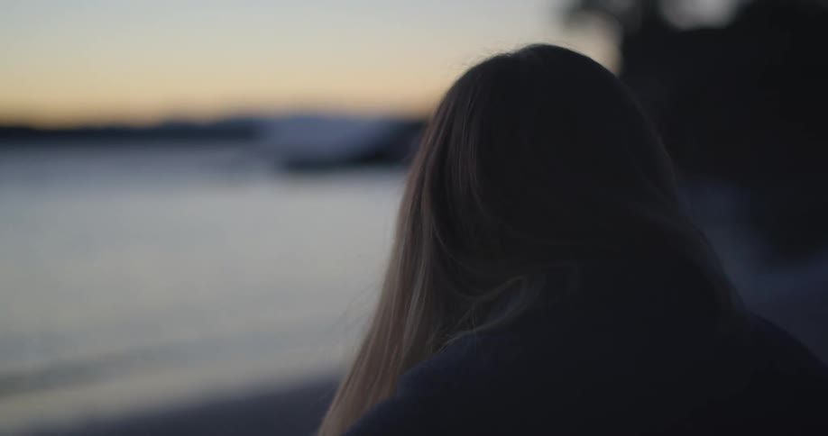 A woman is sitting by the beach at dusk