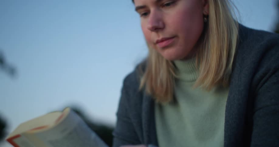 A young woman reads a book while sitting outdoors during the day