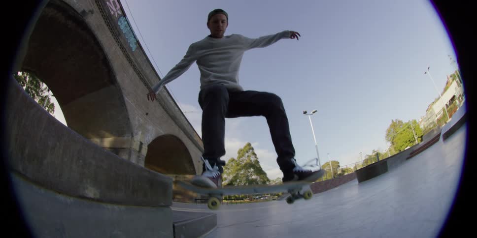 A man does a trick on his skateboard under a bridge
