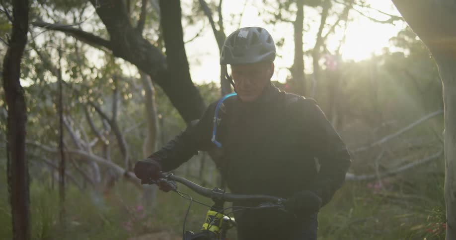 A cyclist pushes a mountain bike through a woodland during the day
