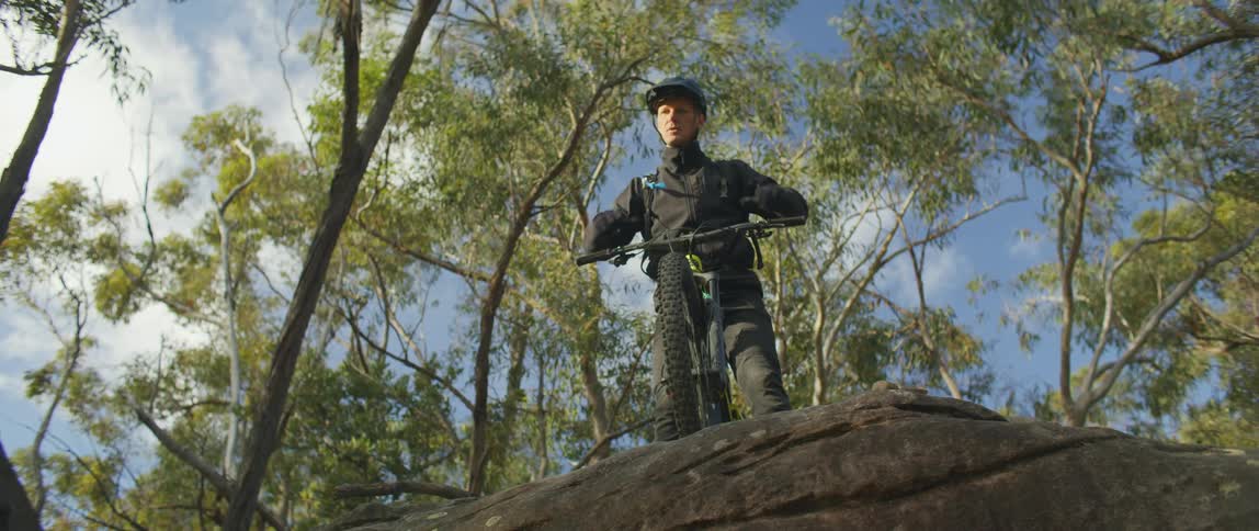 Bicyclist standing on stone drop off under trees fastens helmets as he girds himself
