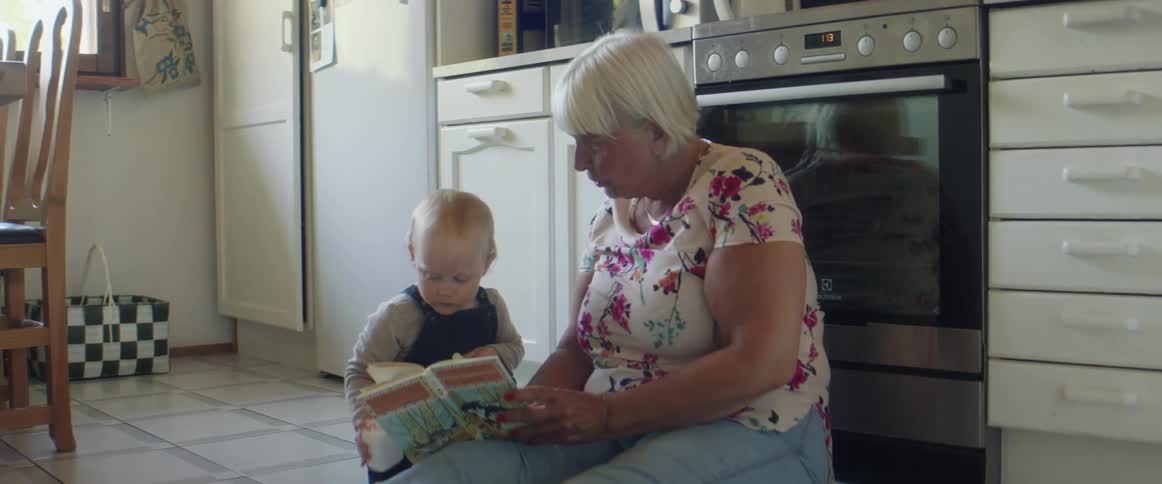 A grandma reads with her grandson while sitting on the kitchen floor