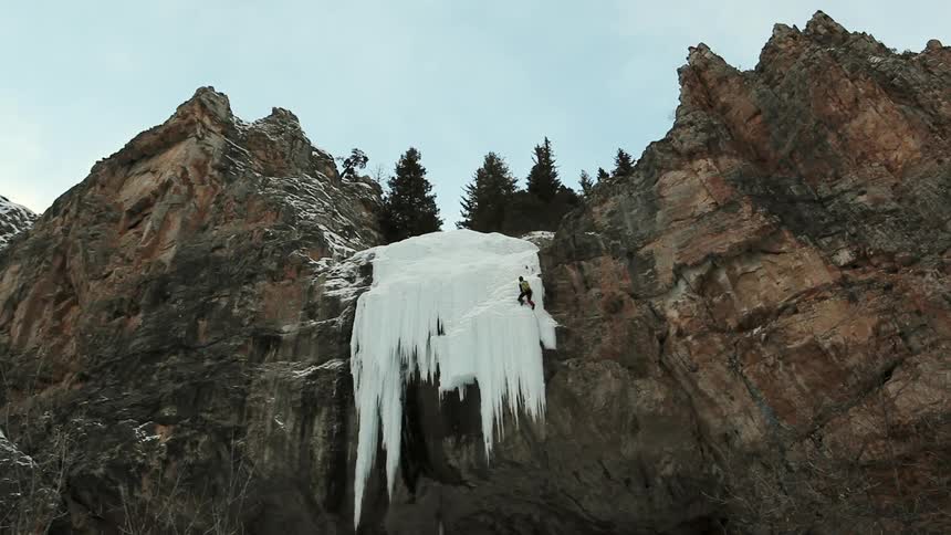 A person climbs up a steep ice and rock formation