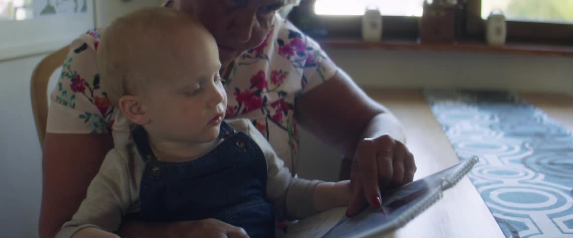 A woman sits with a toddler boy in her lap and they read a book