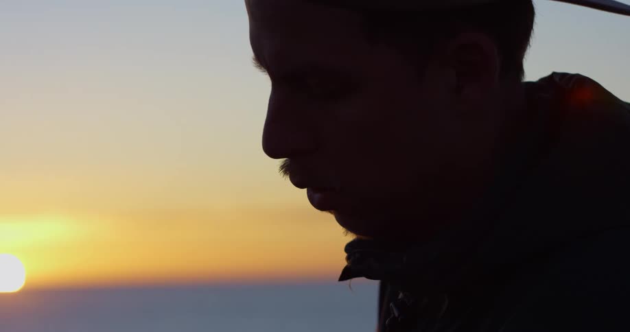 A man is looking down as the sun sets