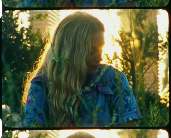 Young blonde woman sitting on the grass in front of the sun at sunset