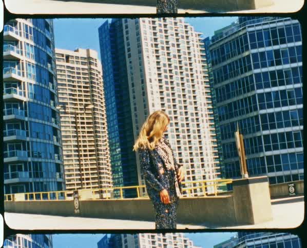 Footage of a woman standing in a downtown city is displayed during the day
