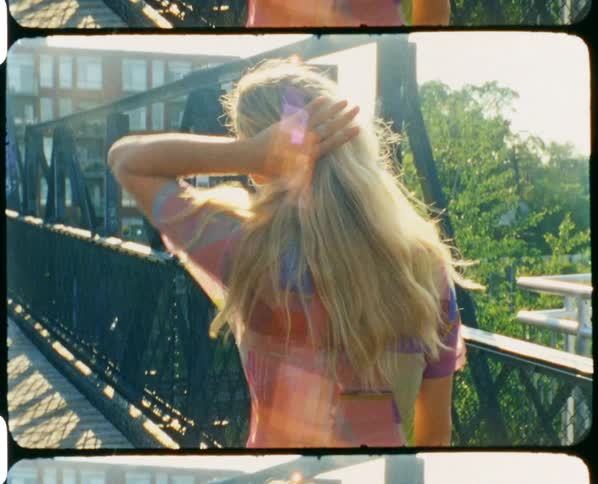 A woman plays with her hair while walking on a pedestrian bridge on a sunny day