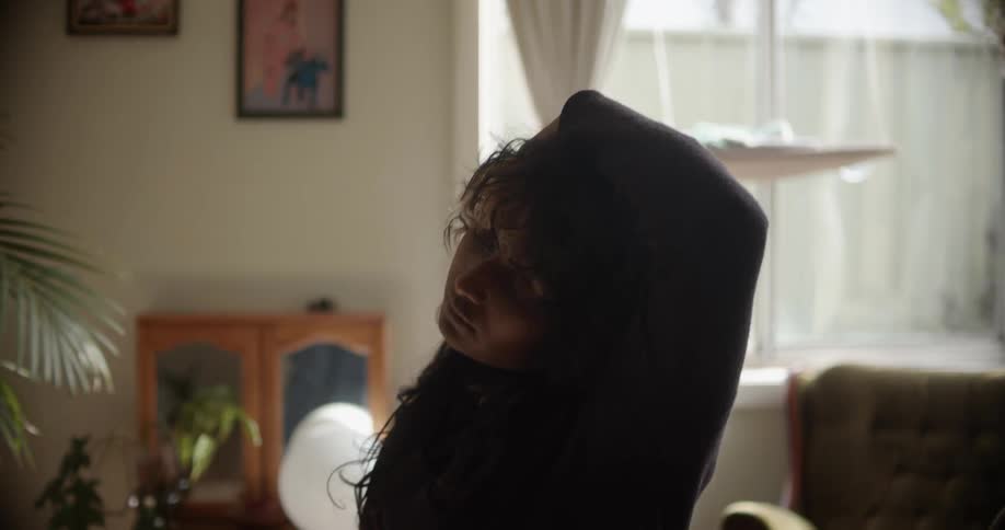 A woman stands in a room with her arm over her head then switches to the other arm