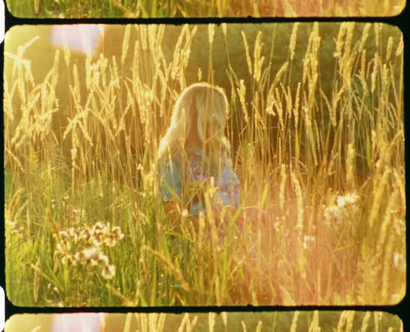 Vintage film of a woman standing in a field of wheat and pulling her hair up off of her neck