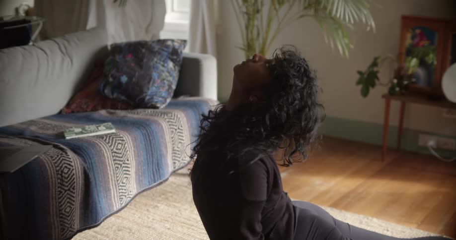 Woman moves through yoga poses on yoga mat near couch