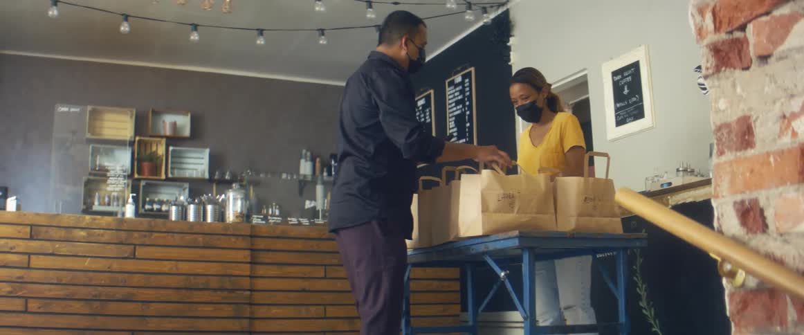 A man walks into a cafe to pick up a togo food order from a female employee