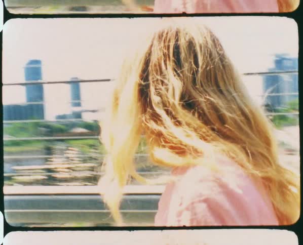 A woman with sunglasses walking in an overpass with buildings the sky and clouds in the background