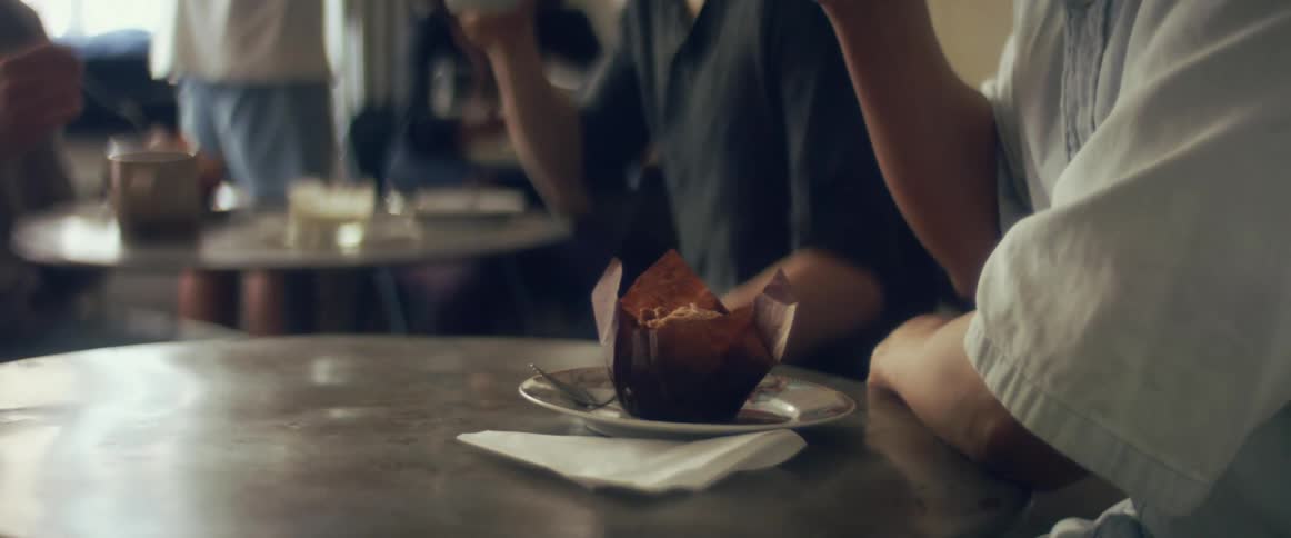 A person drinking orange juice and eating a muffin in a cafe