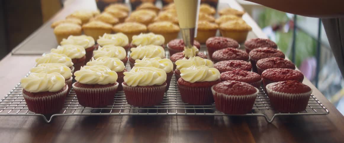 A person putting frosting on a cupcake