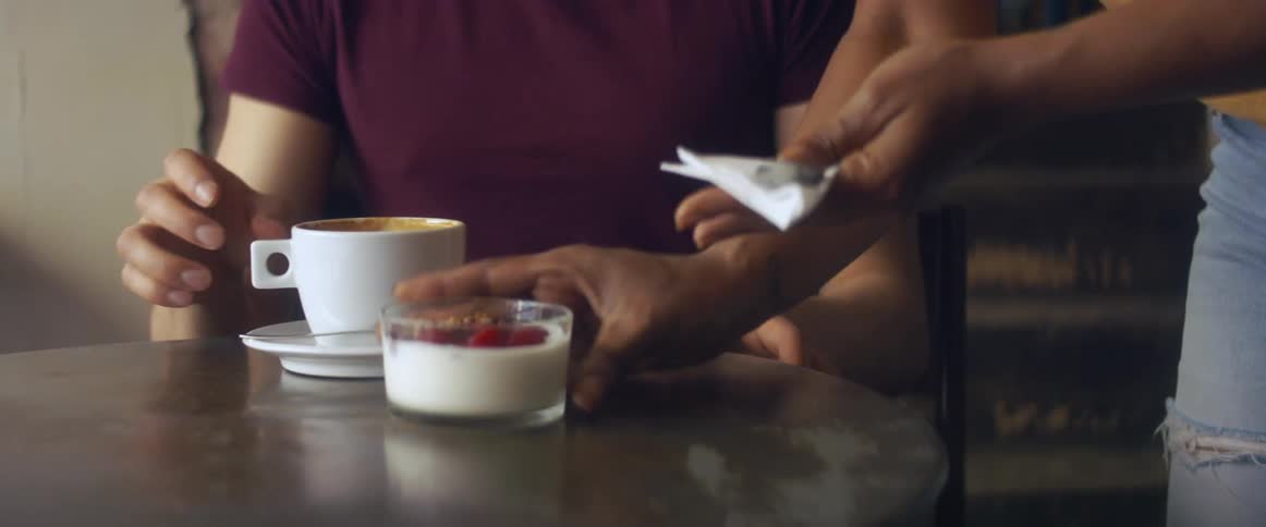 A person handing a cup and a container of yogurt to another person sitting at a table