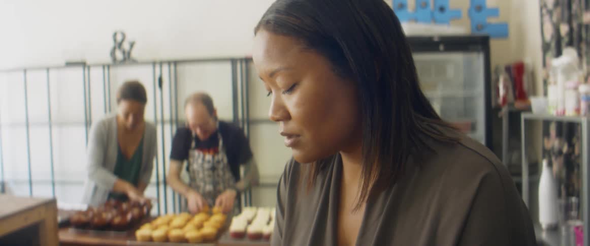 Woman prepares orders on a bakery while workers bring sweets
