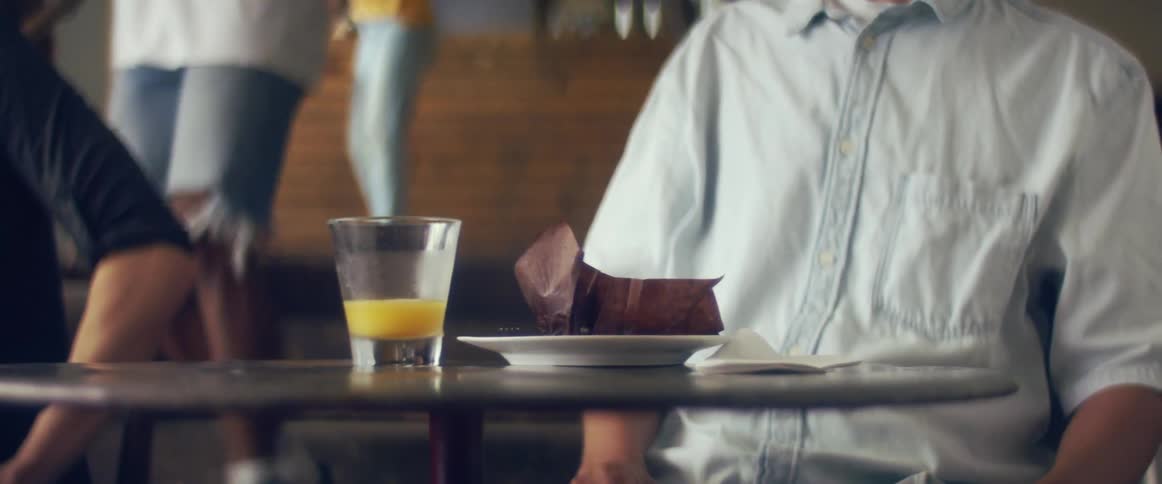 Waitstaff wipes table as customer sits at another table eating and drinking