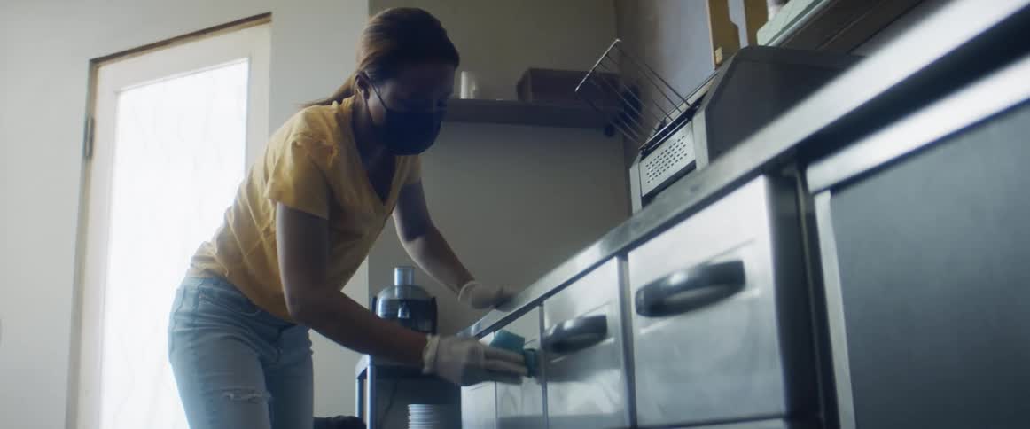A woman in a room with gloves and a sponge cleaning the handle of drawers