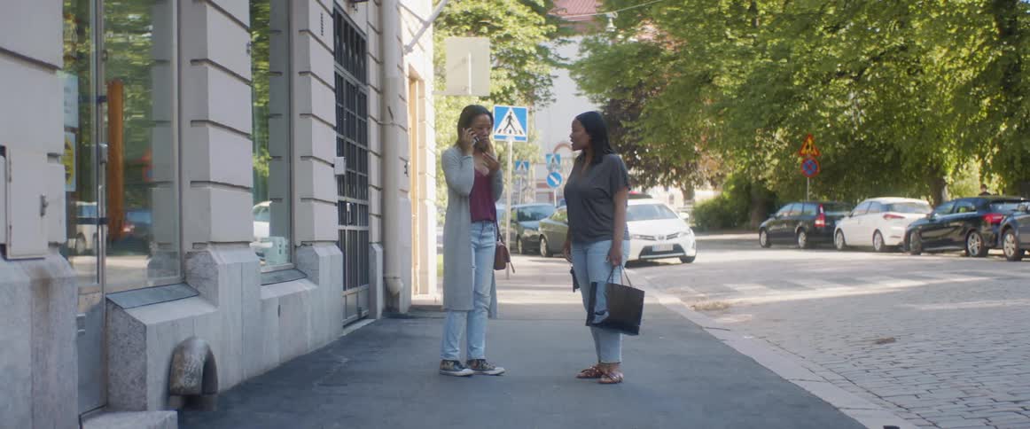 A woman walking down a city sidewalk with a friend stops to answer her phone before finishing her call and hugging her friend