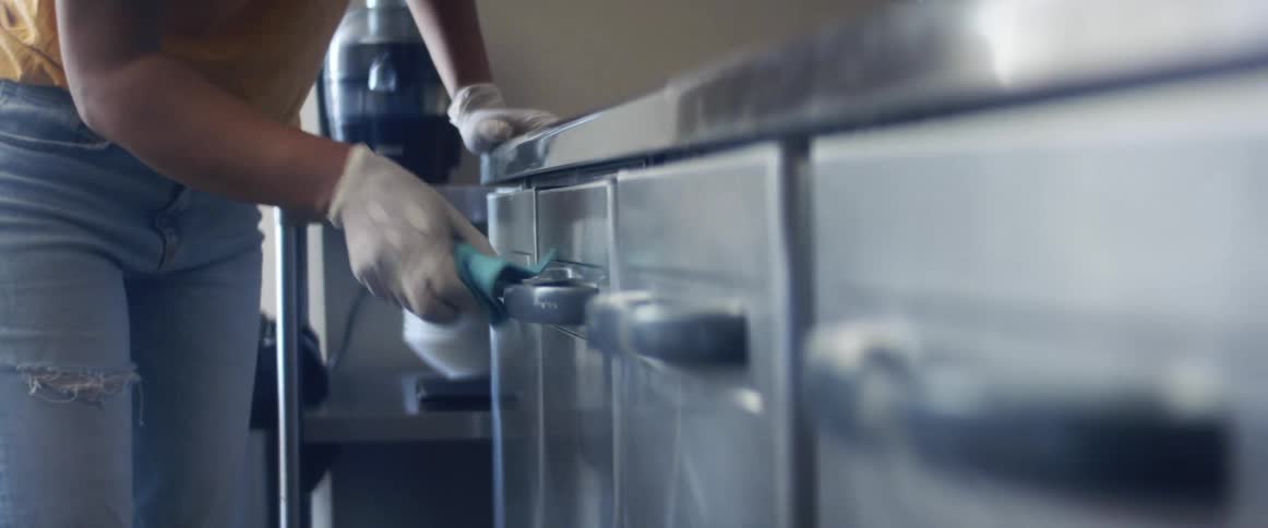 A restaurant employee wipes down the handles of stainless steel cabinets in the kitchen