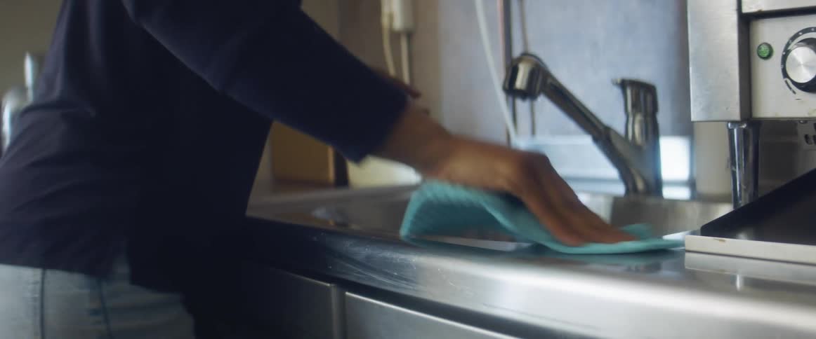 Woman wearing long sleeve shirt cleans sink area and faucet
