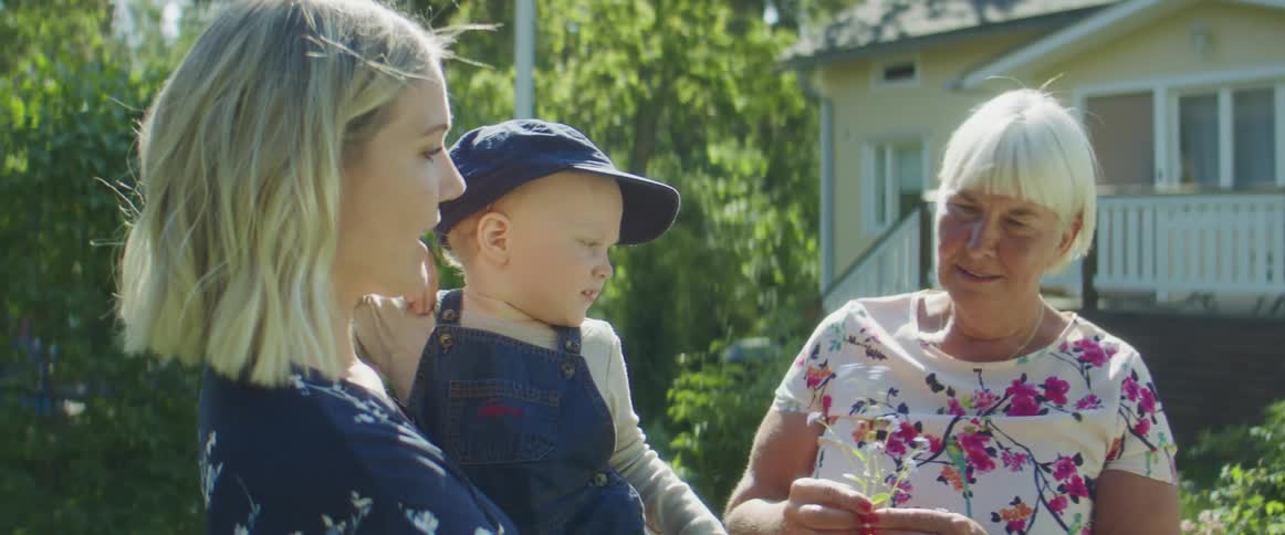 Family stands talking in garden of house smelling flowers