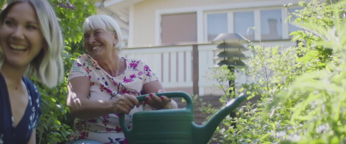 Two women talk and water plants in their yard