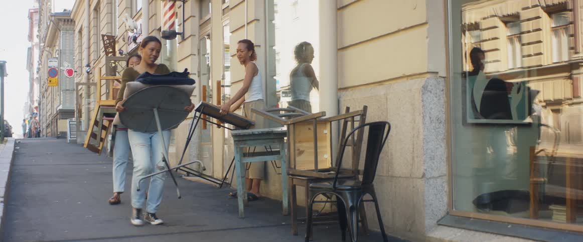 Three women next to a building in a city moving tables and chairs