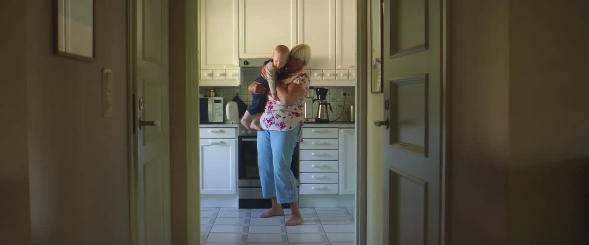 A woman is holding a small boy and then sets him on the floor
