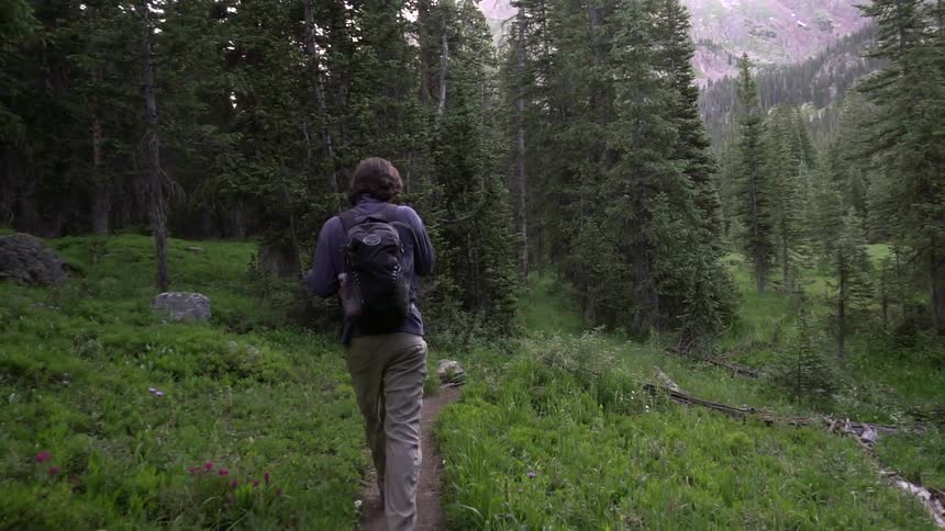 Person hiking a narrow trail wearing a backpack
