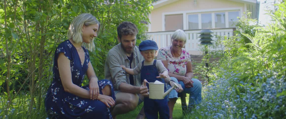 Dad washes his childs hands with water from a watering can in the yard while mom and grandma look on