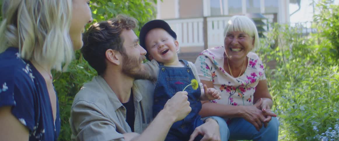 Family sits in garden smelling flower then smiling and laughing