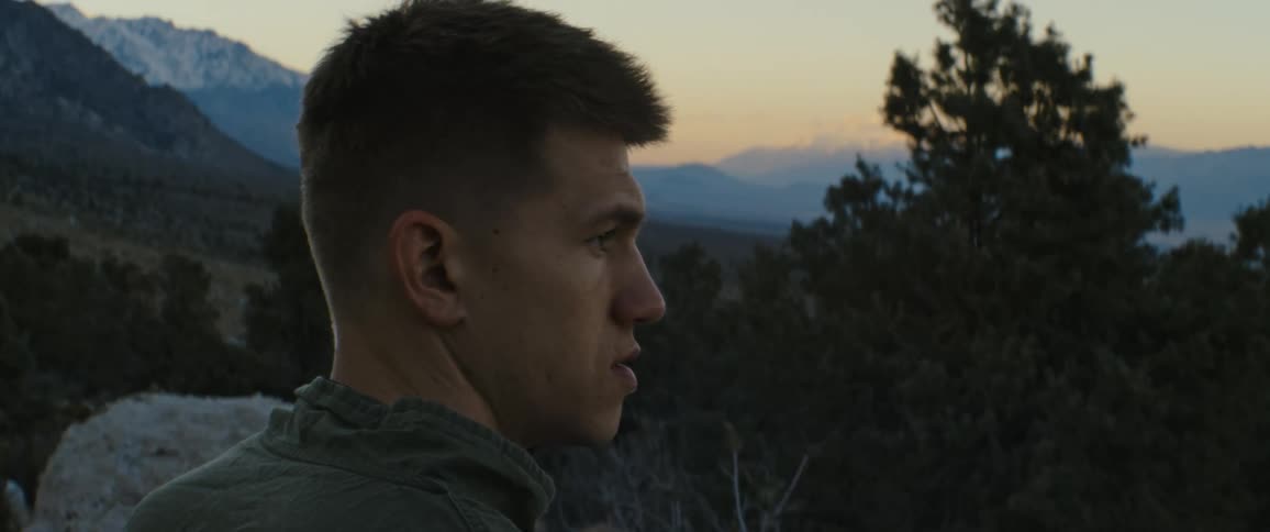 A man standing with trees a mountain range the sky and clouds in the background