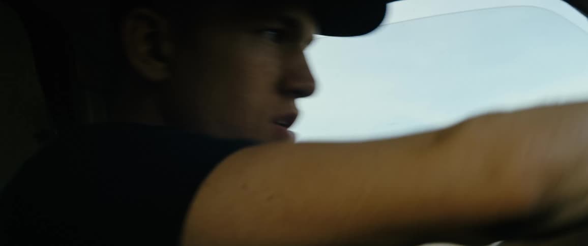 A man with a hat drives a vehicle with the sky and clouds in the background