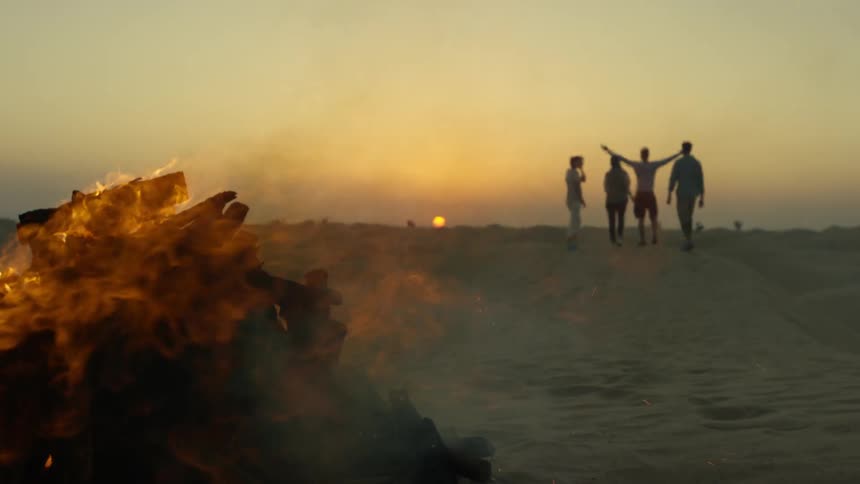 A group of people standing out on the beach near a bonfire
