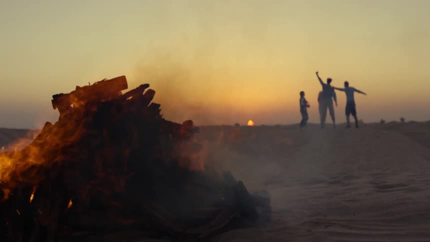 Two men and two women have fun on the beach as a bonfire burns nearby