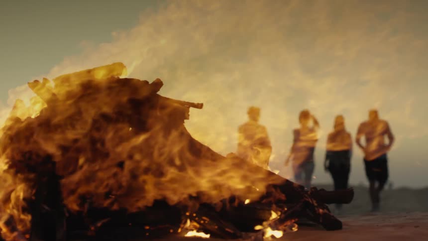 Flames brightly burning from a bonfire as people are walking in the distance