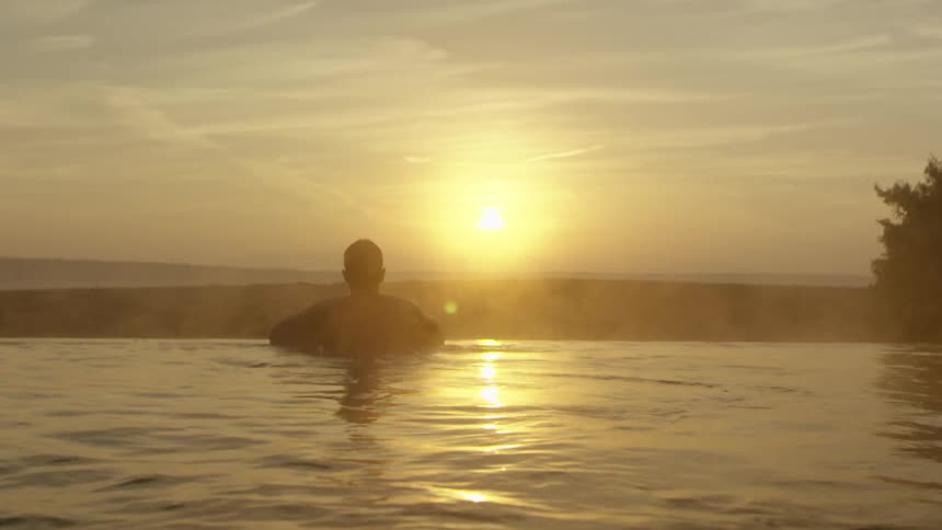 A man in the water is looking at the bright sun setting