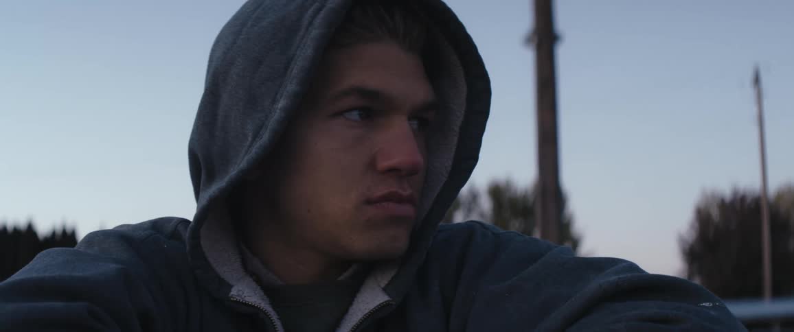 A man wearing a hoodie sits and looks around him