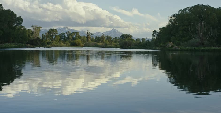 A lake surrounded by trees and the clouds in the sky are reflecting onto the water