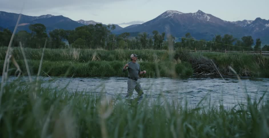 Man fly fishing while standing on a river near the mountains at morning